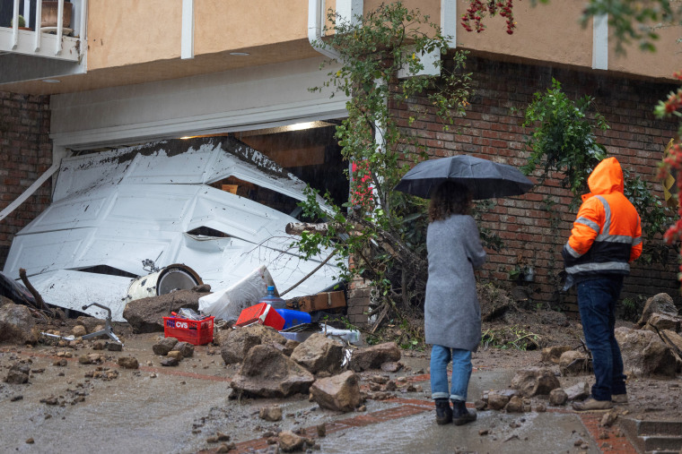 People stand near a garage that a landslide and flash flood smashed through in a hillside residential neighborhood in the Studio City section of Los Angeles, California, on February 5, 2024. 