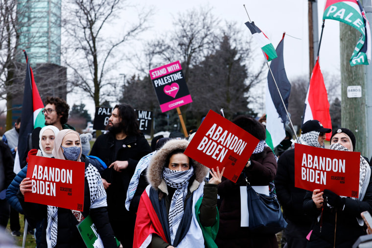 Pro-Palestinian protesters carry signs read, "Abandon Joe Biden" and "Stand with Palestine."