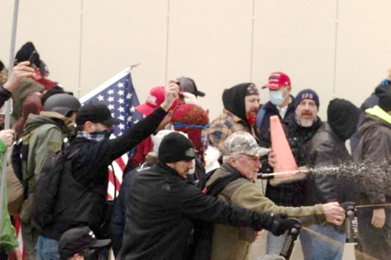 Aaron Sauer, in black baseball cap and a blue and white face covering, holds pepper spray during the Capitol riots on Jan. 6, 2021.