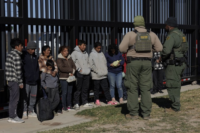 U.S. Border Patrol agents guard migrants that crossed into Shelby Park as they wait to be picked up for processing in Eagle Pass, Texa