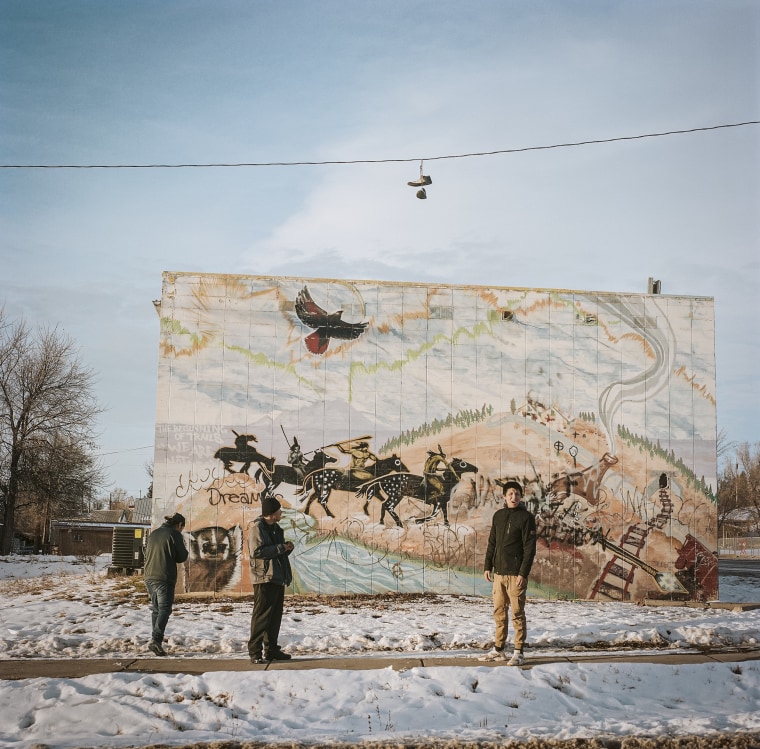Men stand next to a mural in central Lame Deer on the Northern Cheyenne Reservation