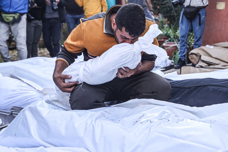 A Palestinian man holds a child's body in a body bag in his arms as he mourns at Nasser Hospital.