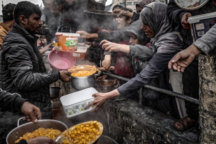 Palestinian children wait in line to receive food prepared by volunteers.