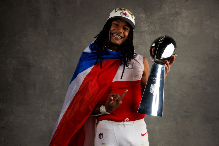 Isiah Pacheco wears the Puerto Rican flag as he points to the trophy while posing for a portrait.