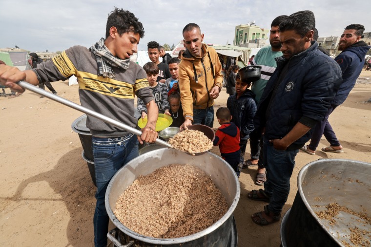 Palestinians with children wait to receive food cooked by a charity kitchen amid shortages of food supplies in Rafah, southern Gaza,  on Feb. 13, 2024. 
