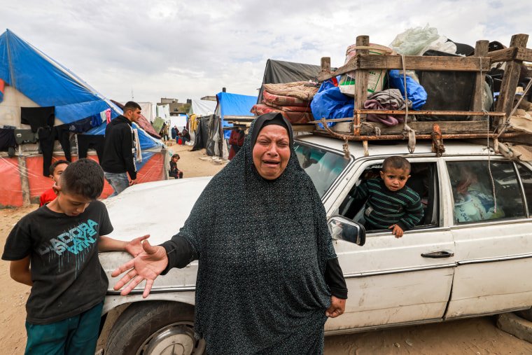 A woman cries in front of a car loaded with items to flee
