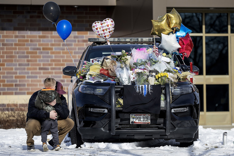 Zach Osterberg, of the Savage Fire Department, hugs his son Lincoln as they paid their respect at three memorials in front of the Burnsville Police Department in Burnsville, Minn., Monday, Feb. 19, 2024. Two police officers and a first responder were shot and killed early Sunday and a third officer was injured at a suburban Minneapolis home in an exchange of gunfire while responding to a call involving an armed man who had barricaded himself inside with family. 