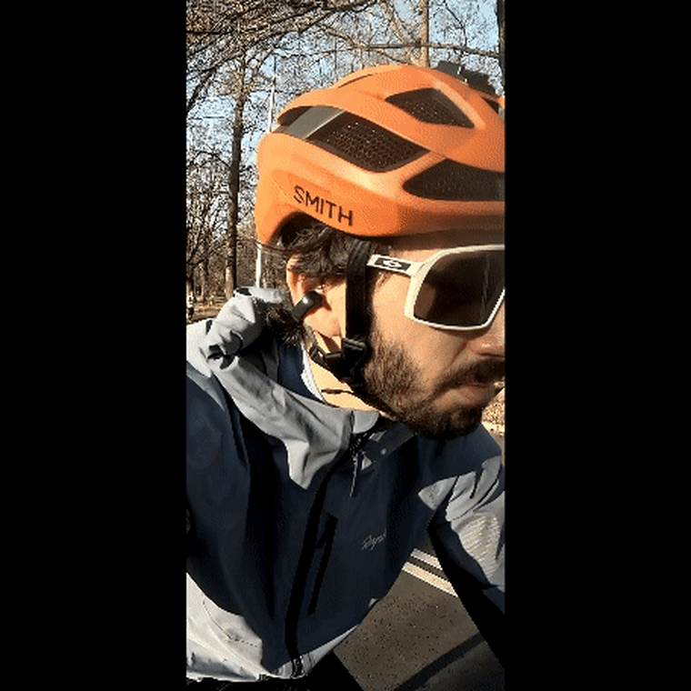 Close-up of the reporter biking in a park, wearing the Bose Ultra Open Earbuds, sunglasses, and a bike helmet.