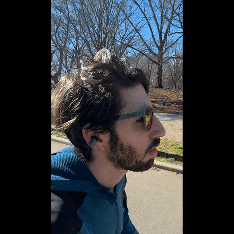 Close-up of the reporter running outdoors in a park with the Bose Ultra Open Earbuds and a pair of sunglasses on.