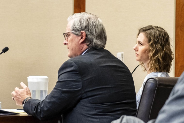 Franke sits in a courtroom, clad in a prison jumpsuit next to her lawyer, an older white man in a dark grey suit.
