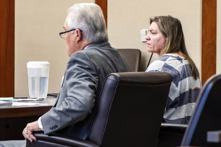 Hildebrandt sits in a courtroom, clad in a prison jumpsuit next to her lawyer, an older white man in a grey suit.