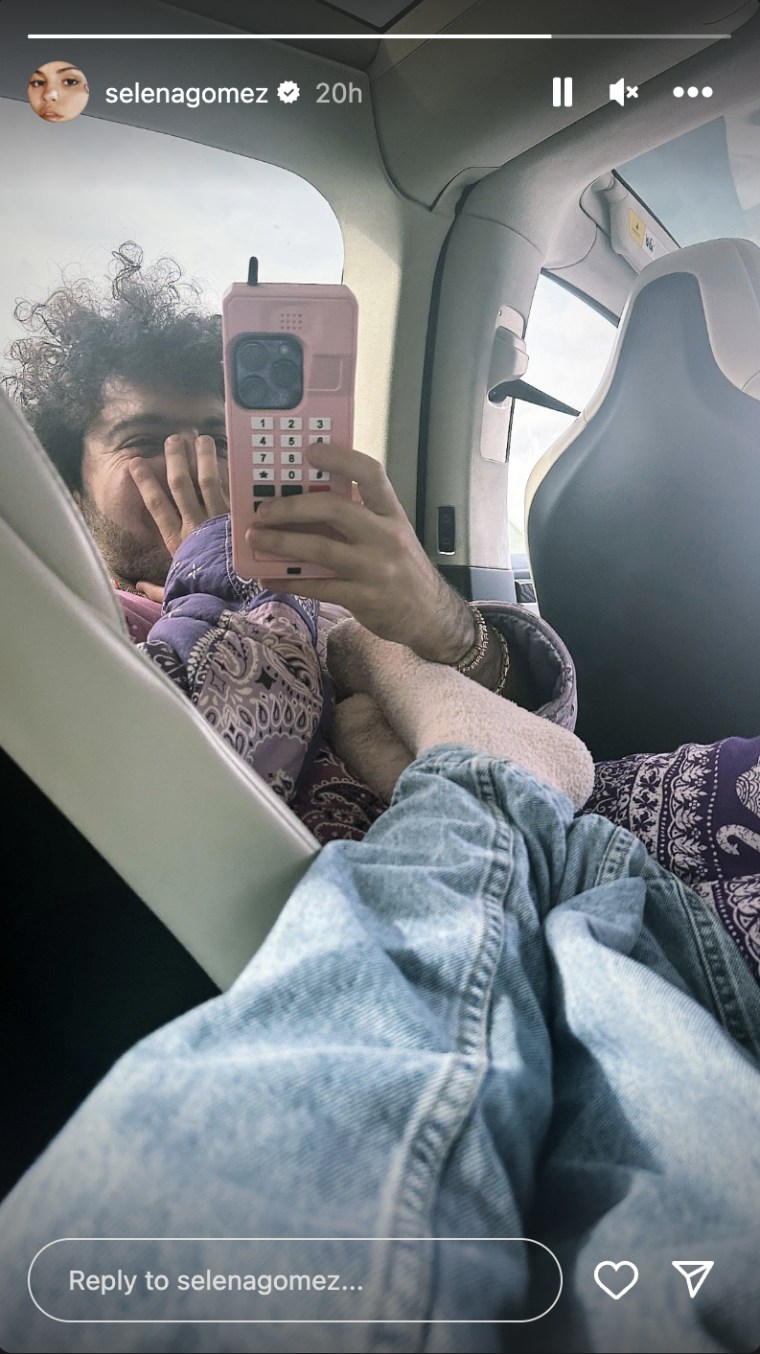 Gomez rubs her feet in fuzzy socks on Benny Blanco inside a vehicle. He's holding a pink iphone.