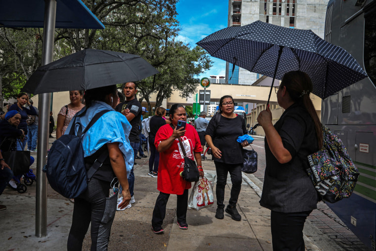 People stand under umbrellas while waiting for a bus during a heatwave in Miami, Florida, on June 26, 2023.