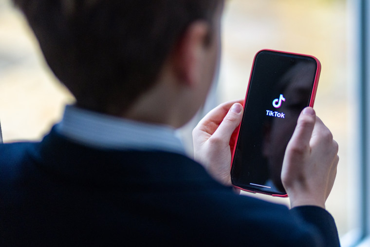 Boy looks at an iPhone screen showing TikTok logo