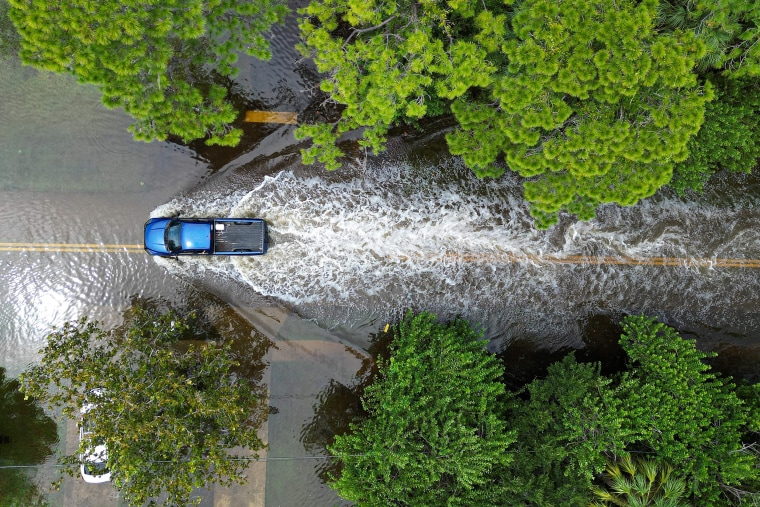An aerial view of a vehicle driving along a flooded street.