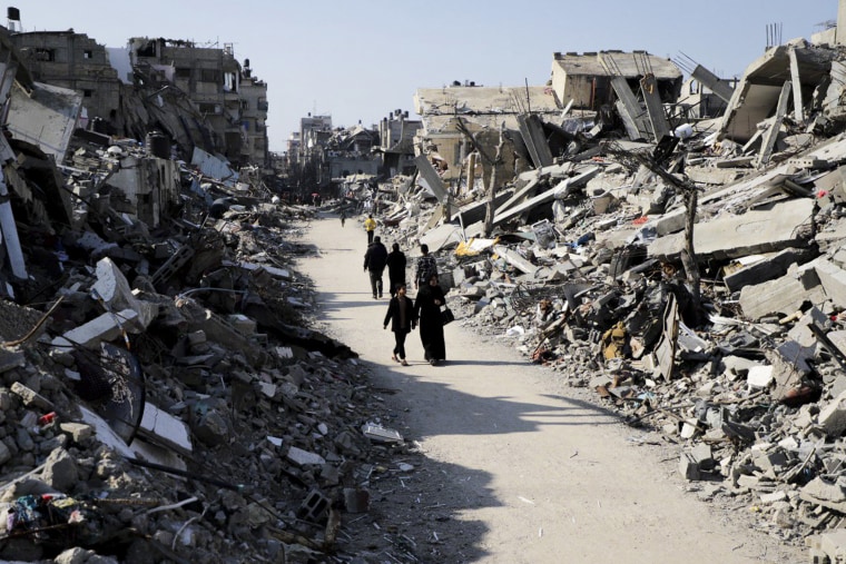 Palestinians walk through the destruction from the Israeli offensive