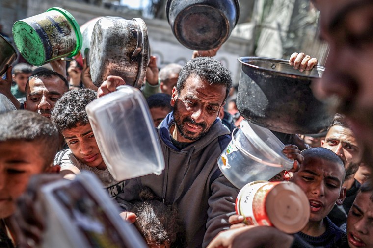 Palestinian people with empty pots receive food distributed by charity.