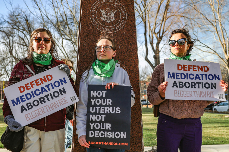 Three members of the Women's March group protest in support of access to abortion medication