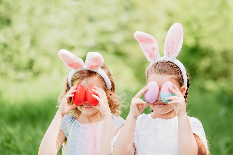 Group Of Children Wearing Bunny Ears Running To Pick Up colorful Egg On Easter Egg Hunt In Garden.