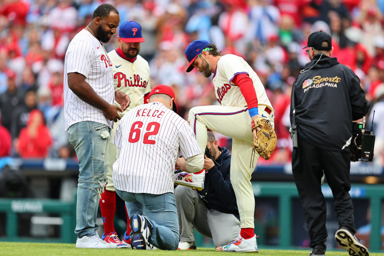 Jason Kelce former Philadelphia Eagle player throws out the ceremonial first pitch autographs the Under Armour cleat of Bryce Harper (3) of the Philadelphia Phillies prior to the game against the Atlanta Braves on March 30, 2024 at Citizens Bank Park in P