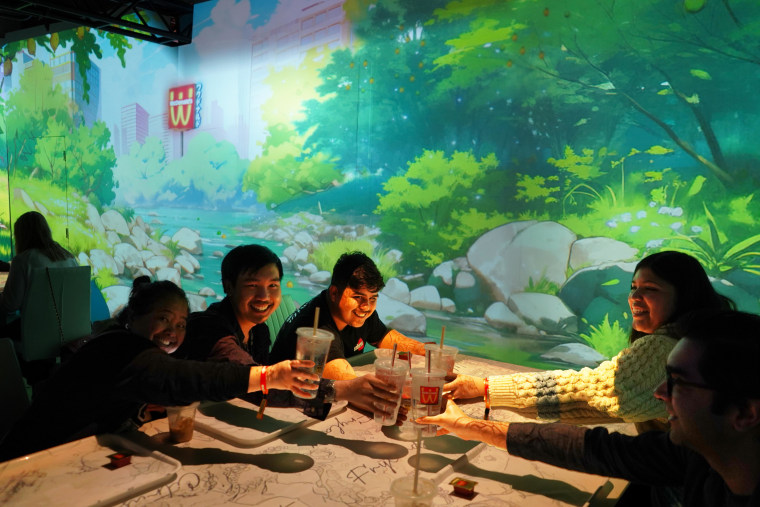 A group of diners cheers with their cups of Sprite over a white table with a projected map on it.