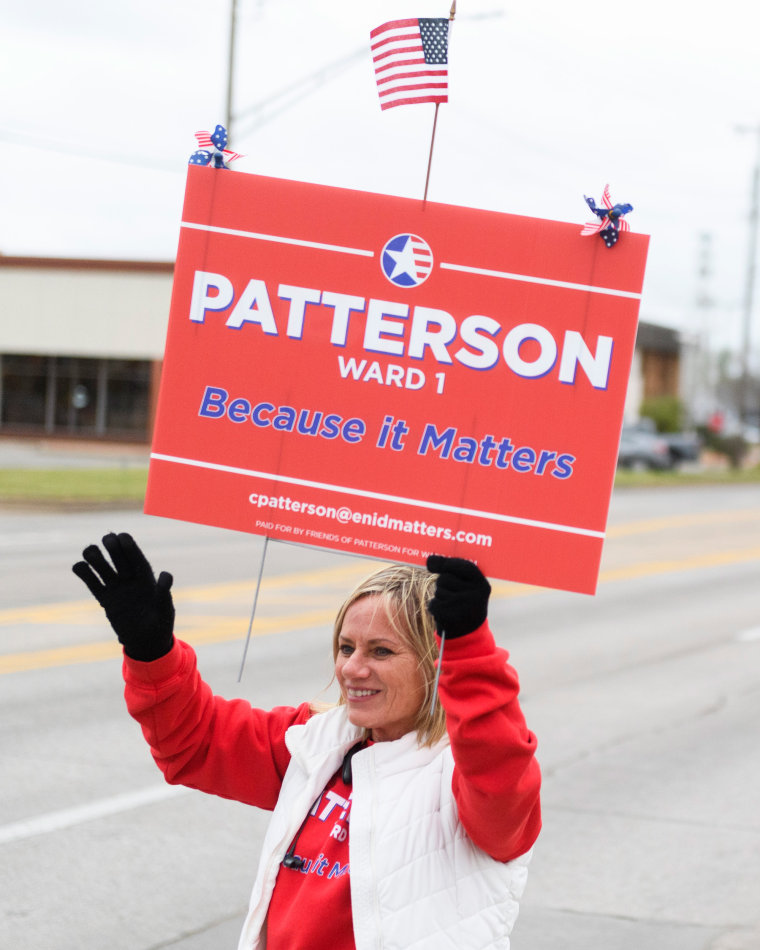 Cheryl Patterson waves while holding a campaign sign.