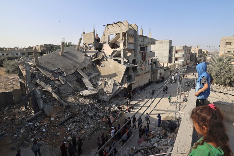 جوانان فلسطینی در 2 آوریل 2024، پس از بمباران شبانه اسرائیل، بر روی پشت بامی مشرف به ویرانی در رفح در جنوب غزه ایستاده اند.