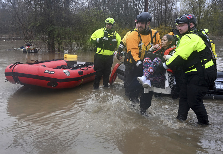 Beaver Falls, Pa., firefighter Jason Tyger, right, gets some help carrying a woman from a boat after she was rescued from her flooded home in Franklin Township, Pa., on April 3, 2024. 