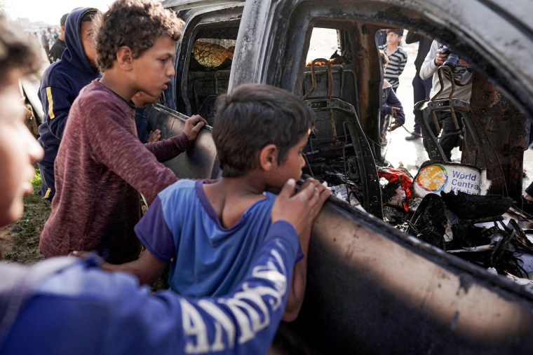 People gather around the carcass of a car used by aid group World Central Kitchen.