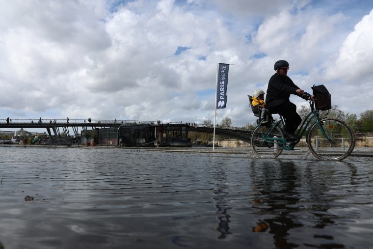 A man carries a child on a bicycle through the flooded docks along the Seine river, near the Passerelle Leopold-Sedar-Senghor bridge in Paris