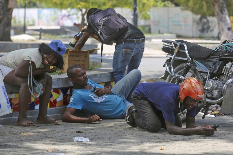 People take cover from gunfire during clashes between police and gangs near the National Palace in Port-au-Prince  on April 8, 2024. 