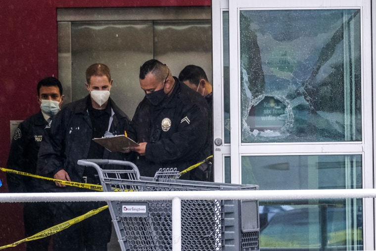 Police officers work near a broken glass door at the scene where two people were struck by gunfire in a shooting at a Burlington store