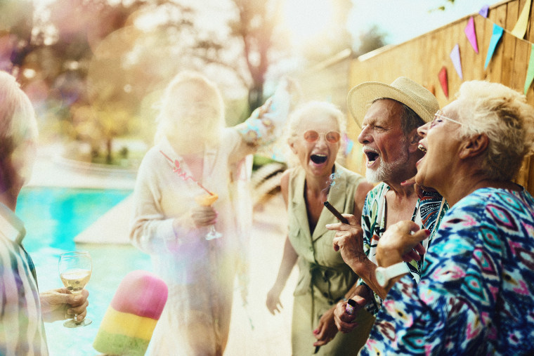 Group of carefree mature friends having fun while dancing and singing on a party during summer day by the pool.