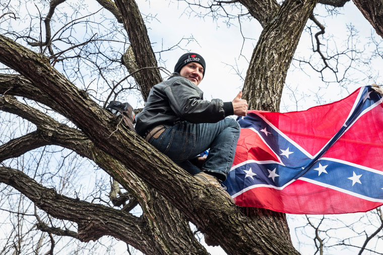 Isreal Easterday perched in a tree holding a Confederate flag