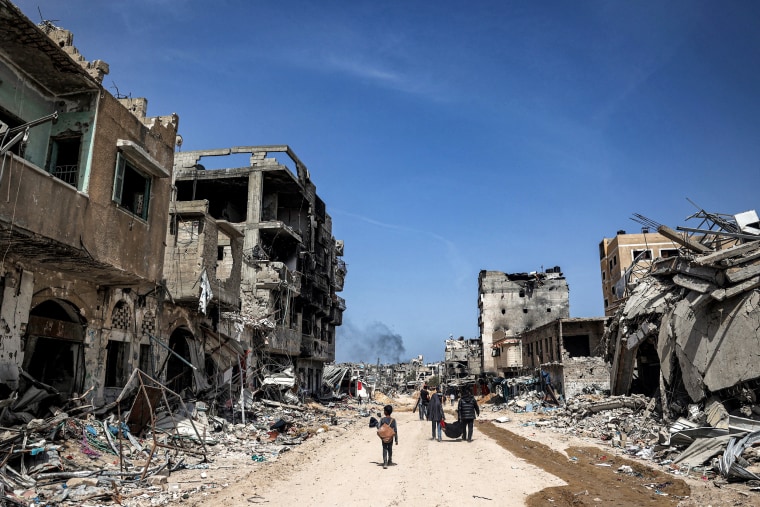 People walk with salvaged items past destroyed buildings in Khan Yunis in the southern Gaza Strip on April 22, 2024.