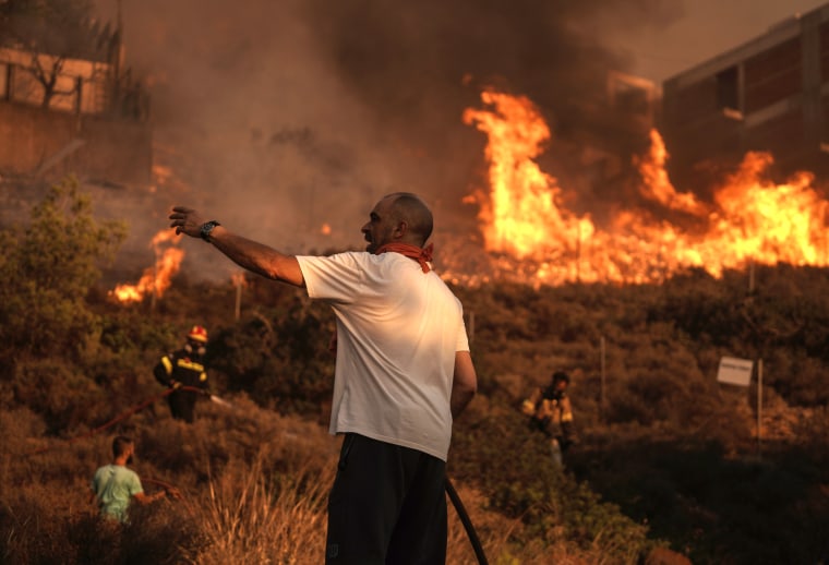Firefighters and volunteers work to extinguish a burning field during a wildfire in Saronida, Greece.