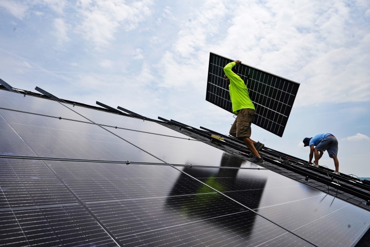 Nicholas Hartnett, owner of Pure Power Solar, carries a panel as he and Brian Hoeppner install a solar array on the roof of a home in Frankfort, Ky., on July 17, 2023.