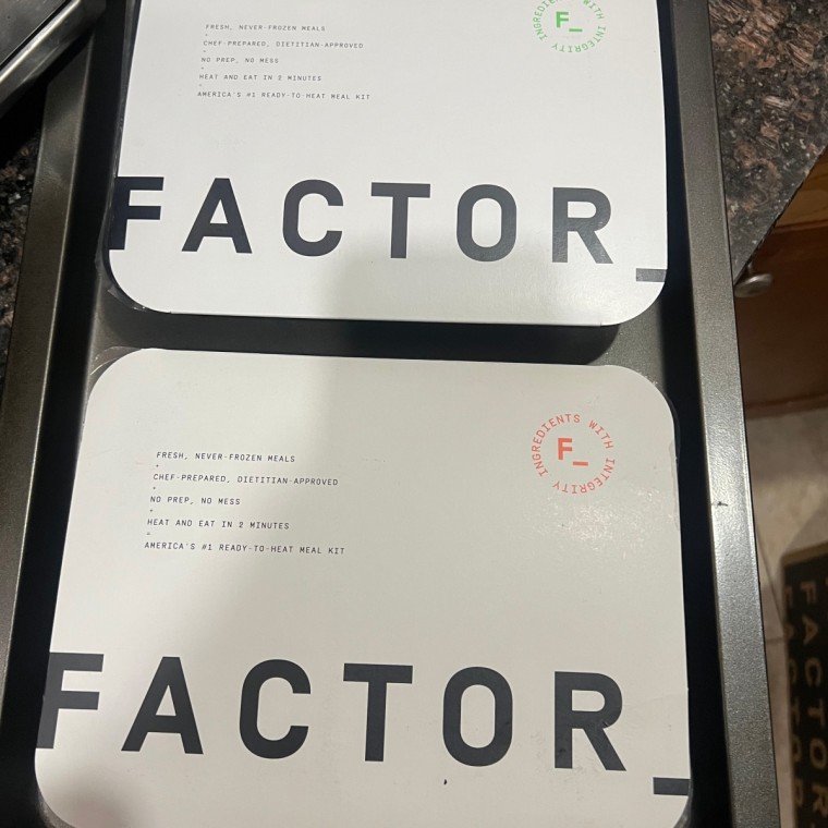 Two Factor meals still in packaging on a pan.