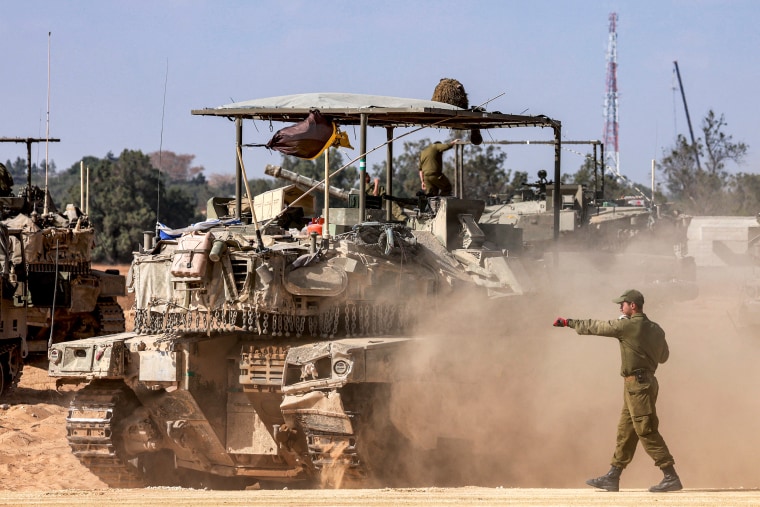An Israeli army soldier gestures behind a moving main battle tank 