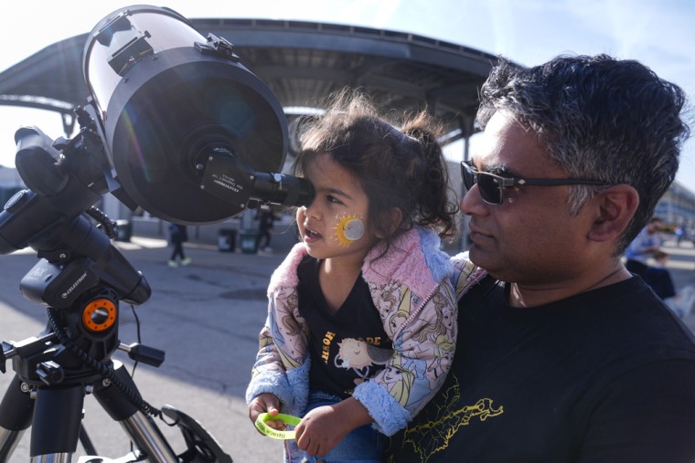 Un hombre junto a su hija observan a través de un telescopio antes del eclipse total en Indianapolis.