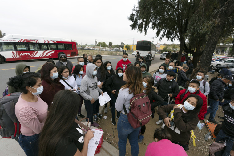 Migrantes escuchan a un voluntario en un estacionamiento después de ser detenidos y procesados para asilo por las autoridades estadounidenses, el viernes 12 de abril de 2024, en San Diego.
