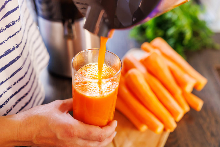 A woman pours fresh carrot juice into glass. Freshly squeezed carrot juice
