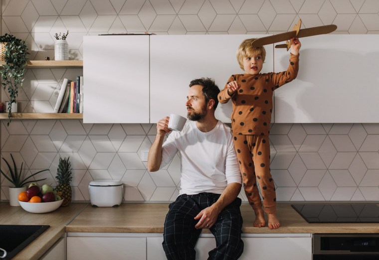 Father sitting on kitchen counter with his little son and having morning coffee.