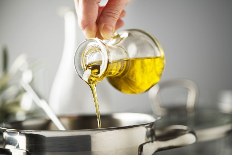 Cooking meal in a pot. Bottle of Extra virgin oil pouring in to pot for cooking meal. Healthy food concept.