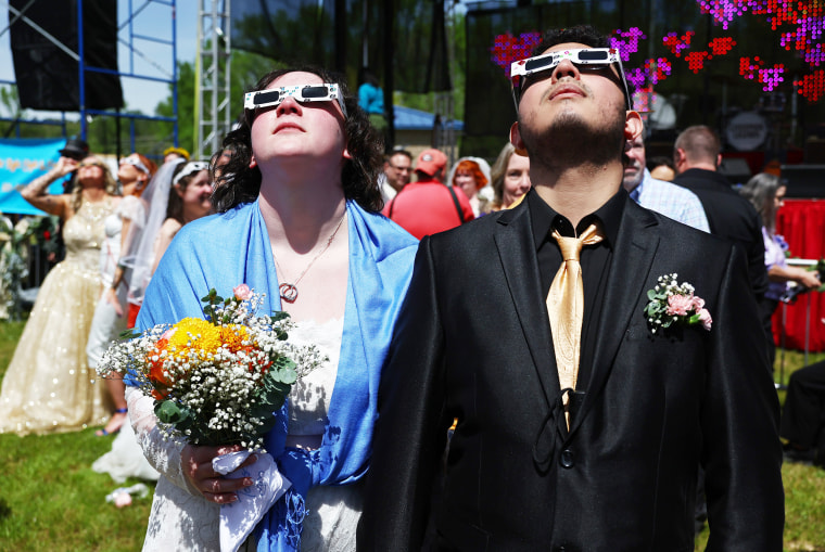 Couples view the solar eclipse during a mass wedding