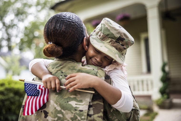 Daughter embracing female U.S. soldier mother in front of home