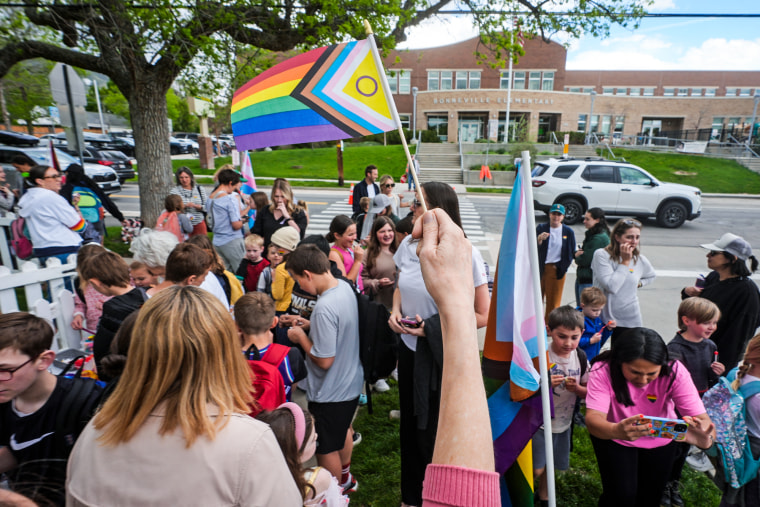 Parents and students are gathered holding pride flags and wearing pride stickers