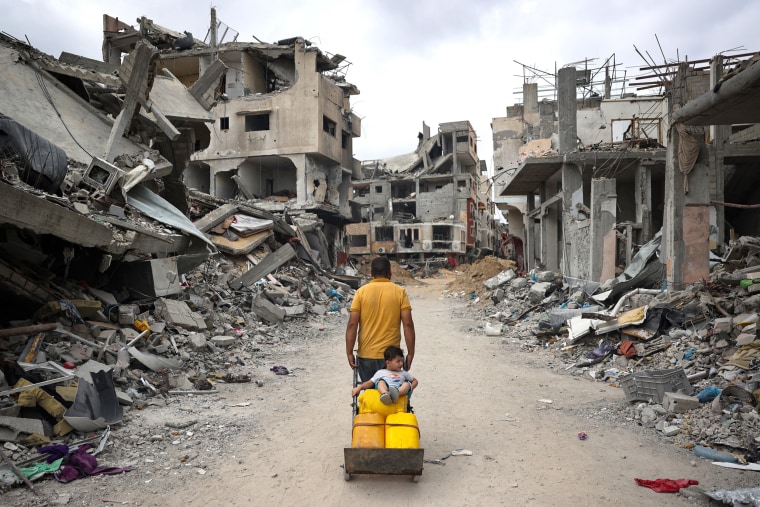 A Palestinian man pulls a cart on a road lined with destroyed buildings in Gaza.