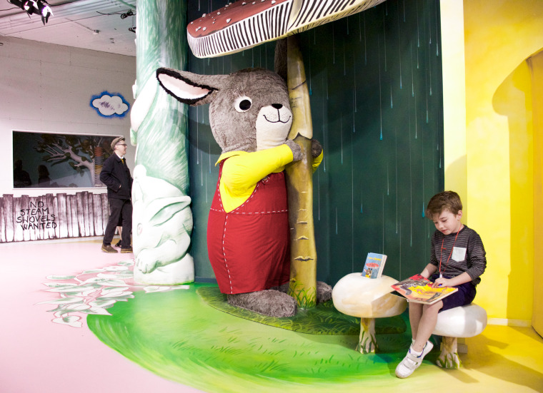 A child reads next to a large bunny sculpture that hugs a mushroom