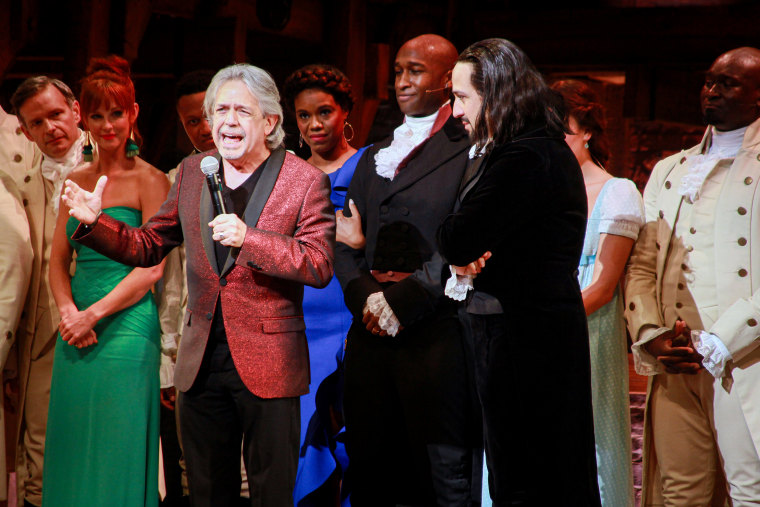 Luis Miranda speaks while Lin-Manuel Miranda and the cast of Hamilton stand on stage.